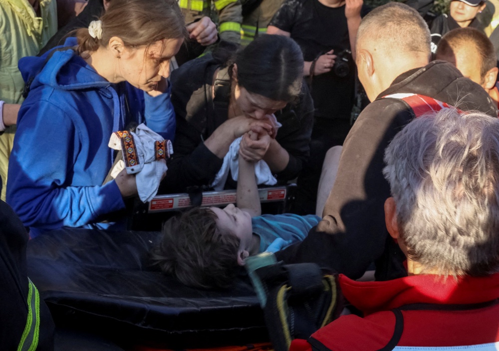 A woman holds the hand of an injured child as medical workers evacuate him at the site of an apartment building hit by a Russian missile strike, (Reuters)