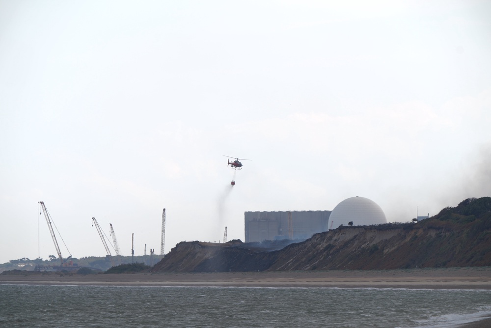 A helicopter flies water collected from the sea to drop on the wildfire close to the Sizewell B nuclear power station (PA)