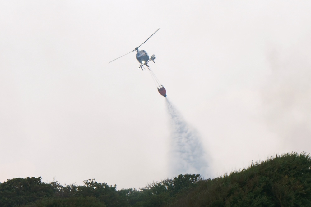 A helicopter flies water collected from the sea to drop on the wildfire at Dunwich Heath, near Leiston, close to the Sizewell B nuclear power station (PA)