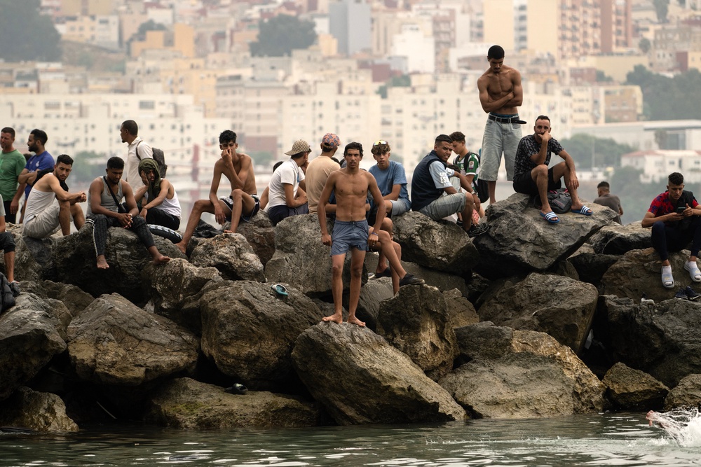 Migrants sit on rocks after swimming through the waters close to the border with Morocco (AFP/Getty)