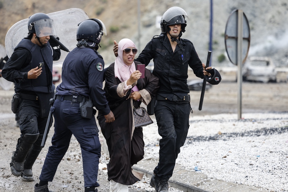A woman is escorted by Moroccan security forces during clashes with migrants attempting to cross into Spain's North African enclave of Ceuta near the town of Fnideq, on the Morocco-Spain borde (AFP/Getty)