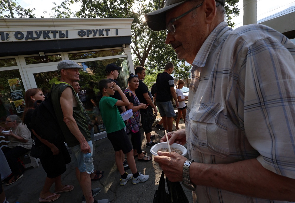 People line up for hot meals at a field kitchen set up by the local authorities in the settlement of Massandra (Reuters)