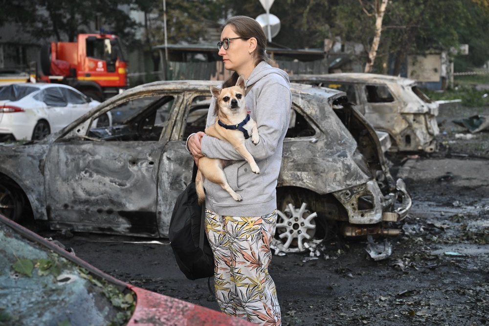 A local resident holds her dog as she examines a broken car parked outside a multi-storey residential building (AFP/Getty)