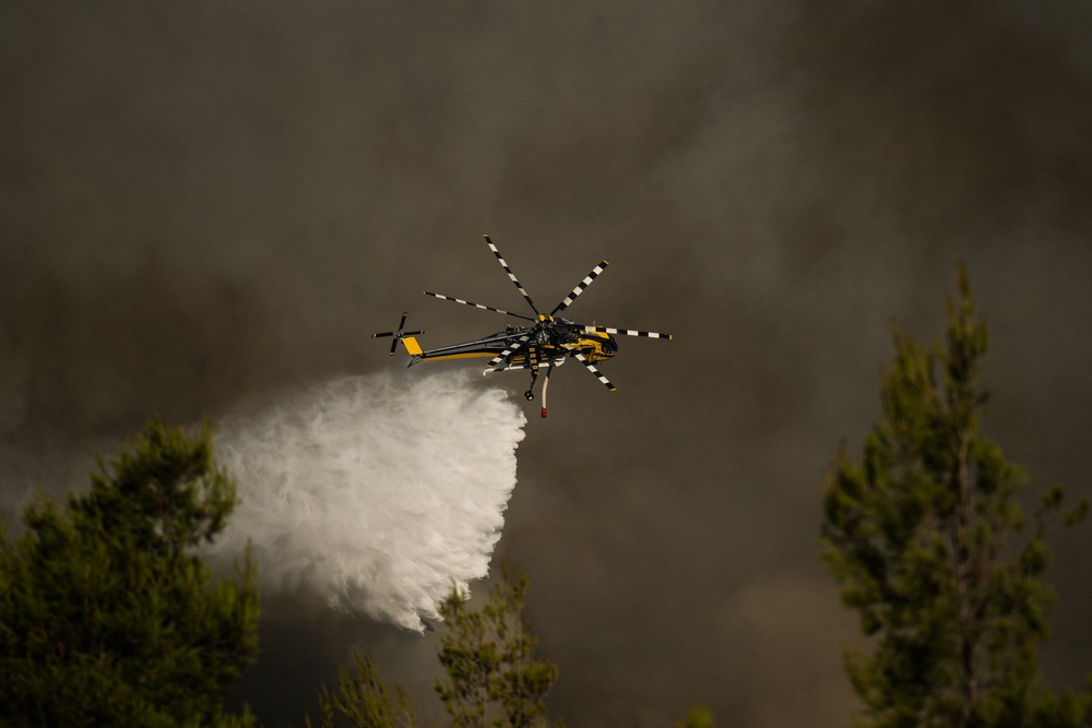 A firefighting helicopter drops water over a cloud of smoke of a wildfire in the area of Porto Germeno, some 70 kilometres (45 miles) (AFP/Getty)