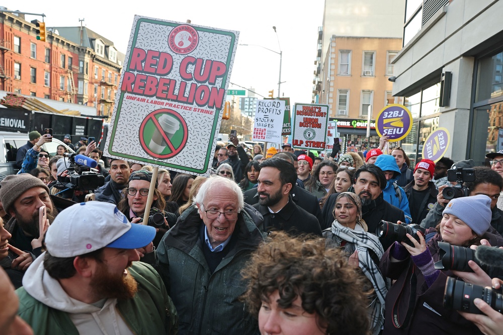 Independent Senator Bernie Sanders holds a ‘Red Cup Rebellion’ sign as New York City Mayor Zohran Mamdani follows behind during a Starbucks worker strike over wages and unfair labor practices in December 2025. Sanders took to X.com in March 2025 to lambaste Starbucks for paying workers low wages while giving CEO Brian Niccol a $96 million compensation package for four months of work in 2024 (AFP/Getty)