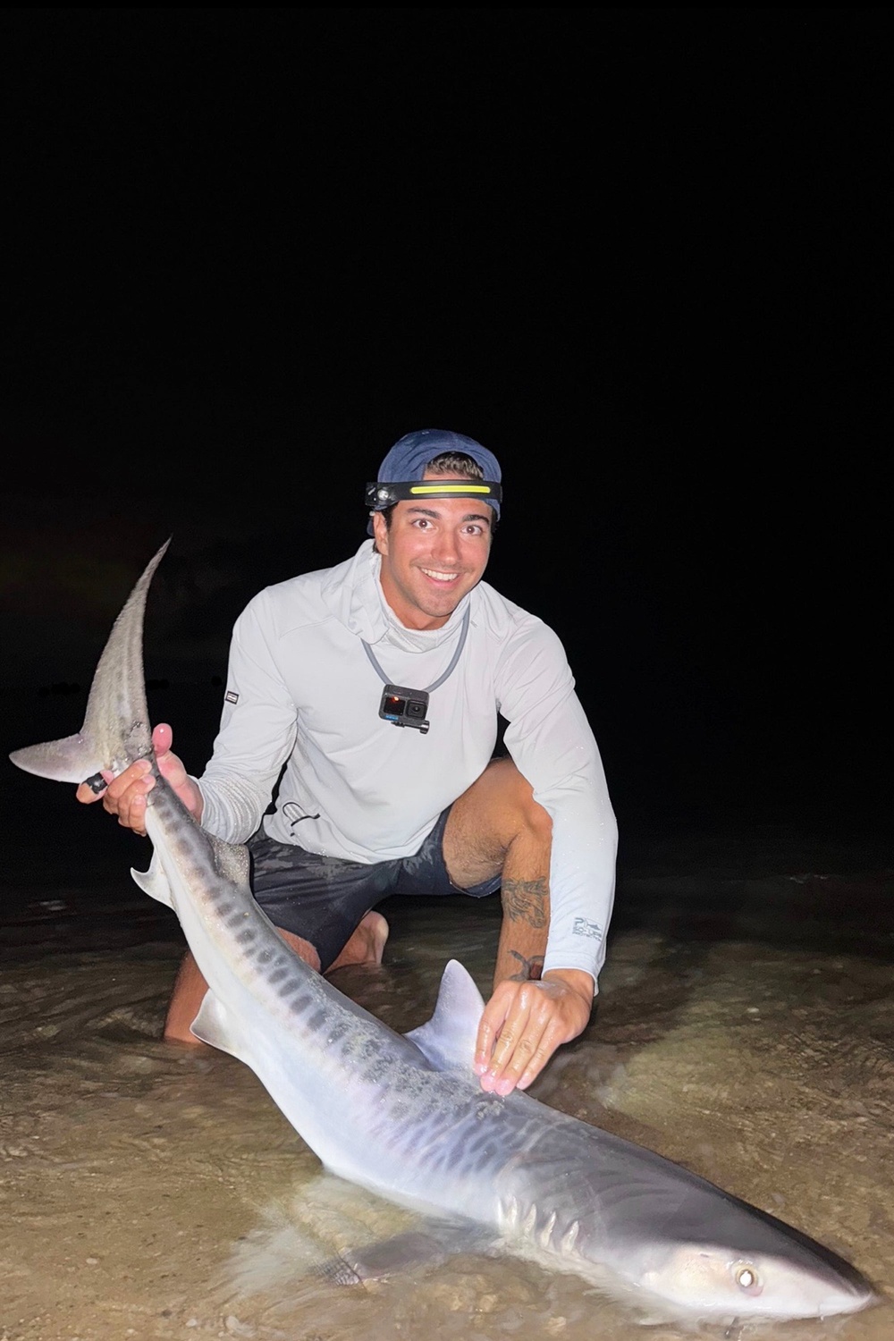 This photo provided by Nelson Rouette shows his brother, Nate Rouette, holding a young tiger shark that they caught off Falmouth Mass., July 23, 2026. (Nelson Rouette via AP) (Nelson Rouette)