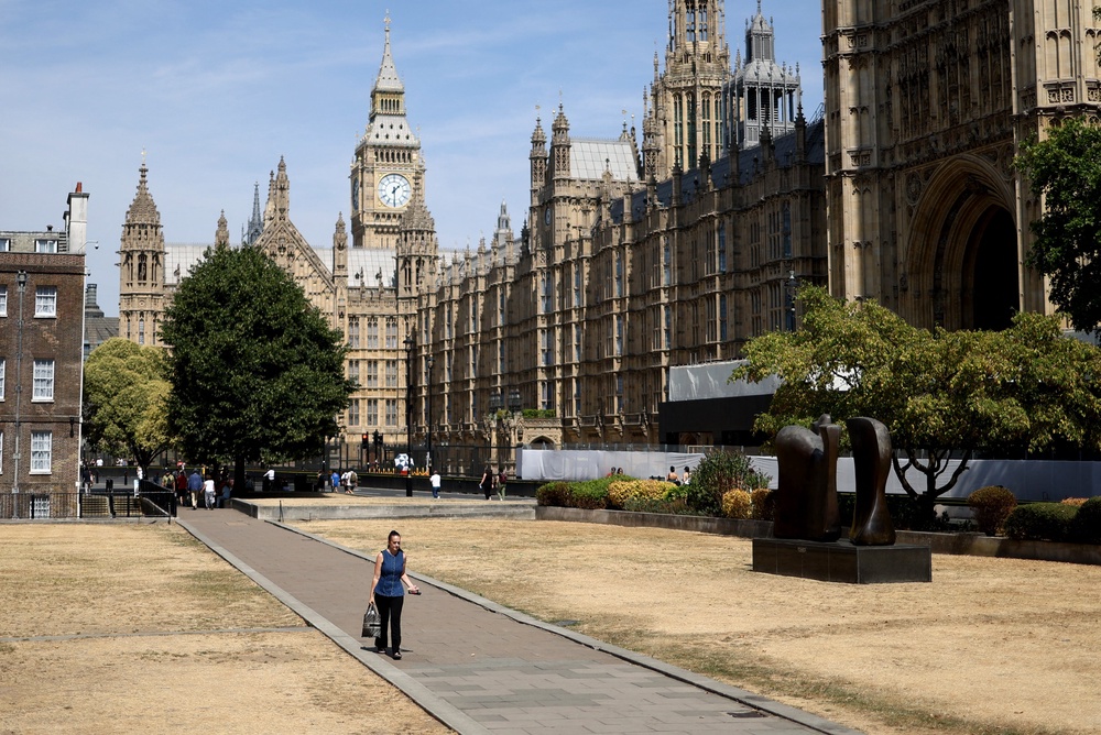 A person walks past sun-scorched grass, backdropped by the Houses of Parliament, after a month without rainfall (AFP/Getty)