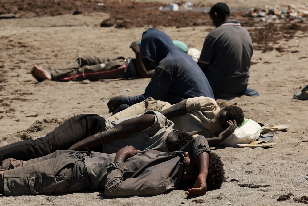 Migrants rest while waiting on a beach (Reuters)