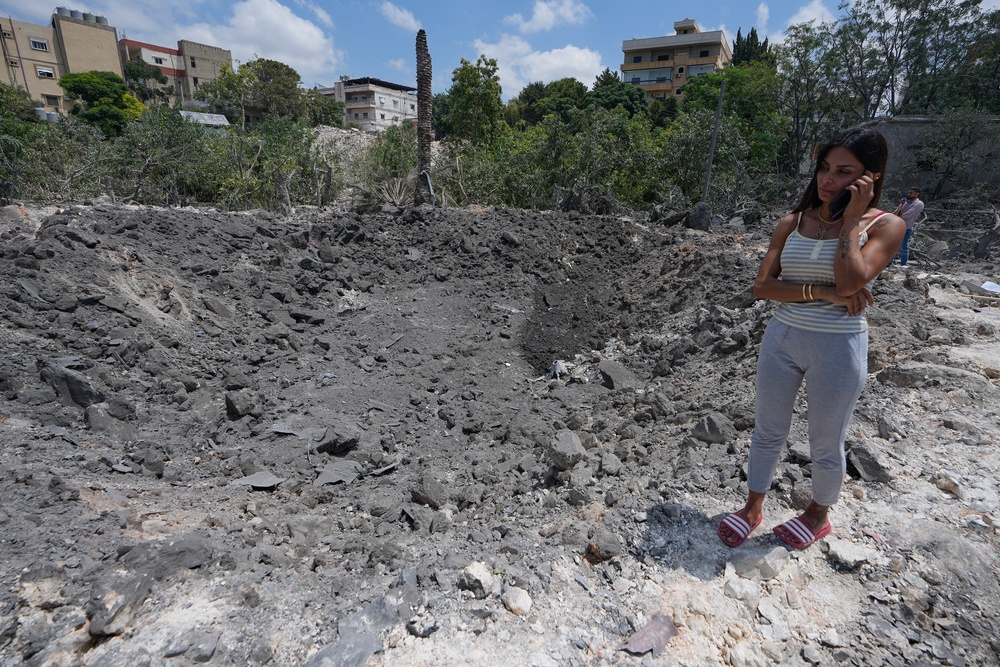 Hanan Jeha speaks on her phone next to a crater on a place of her family house, hit by an Israeli airstrike in Burj al-Shamali village, south Lebanon (AP)