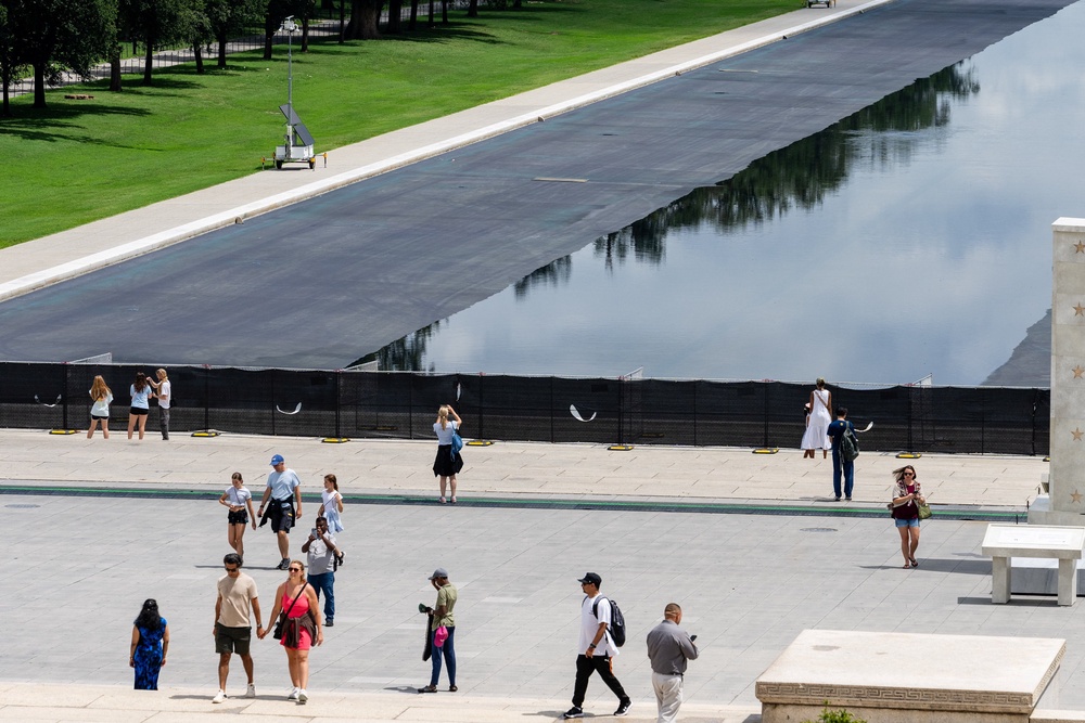 Members of the public can see the Lincoln Memorial Reflecting Pool between gaps in the chain-link fence covered in fabric (Reuters)