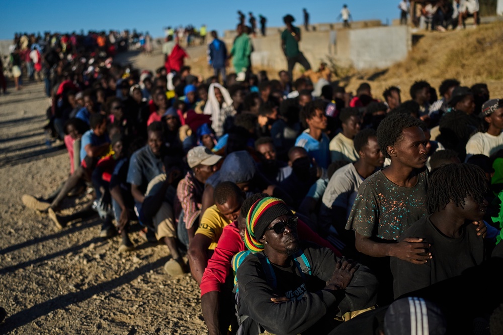 Migrants who crossed from Morocco into Spain line up for food distribution on a beach in the Spanish enclave of Ceuta, Monday, Aug. 3, 2026. (Copyright 2026 The Associated Press. All rights reserved.)