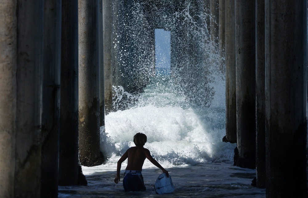 A surfer watches a wave break beneath a pier last month in Huntington Beach, California. Genevieve brought large swells and flooding to Southern California (Getty Images)