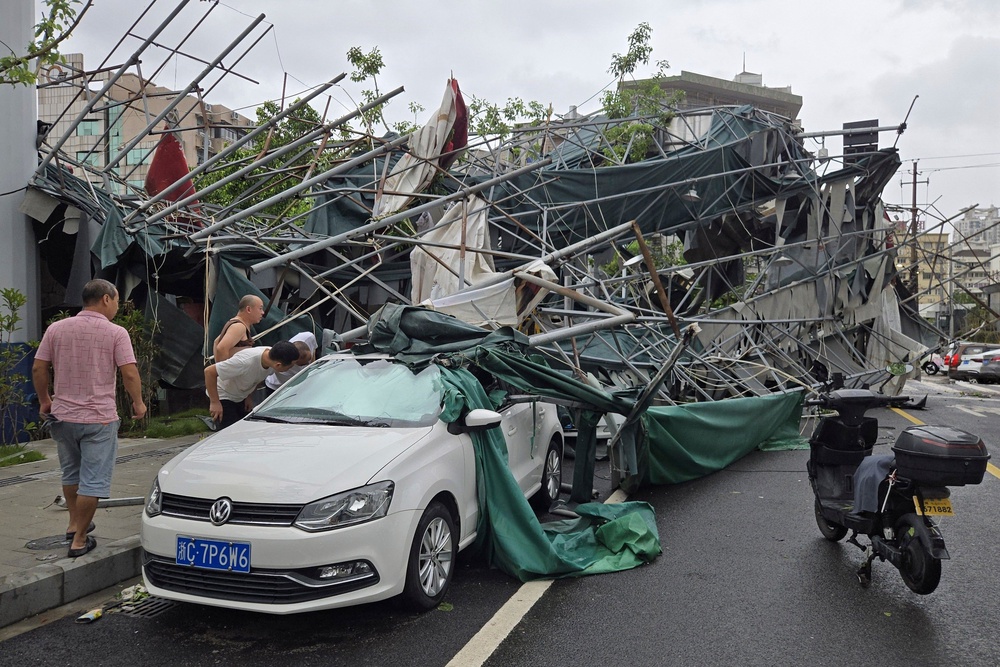 People look inside a car pinned by a fallen scaffolding structure after Typhoon Dolphin (AP)