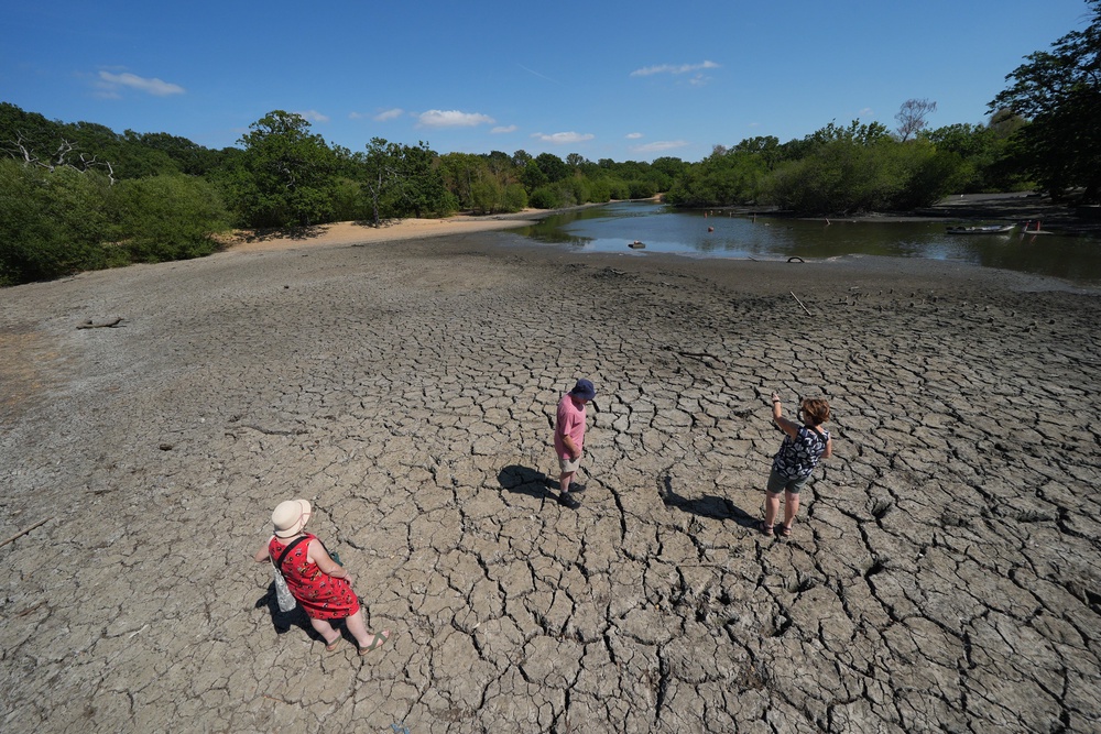 People experiencing the exposed, cracked, and dried mud bed of Hollow Pond in south-east London (PA)