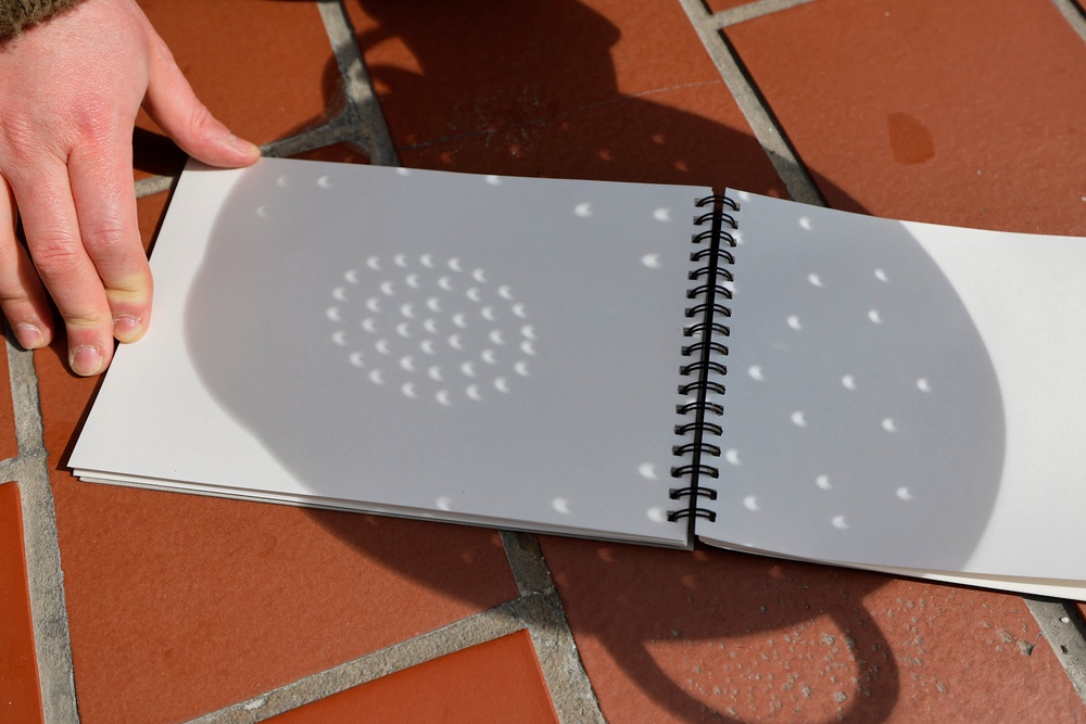 A person uses a colander and paper to see the shadow of a partial solar eclipse from the Top of the Rock at Rockefeller Center on 8 April, 2024 in New York City (Getty)