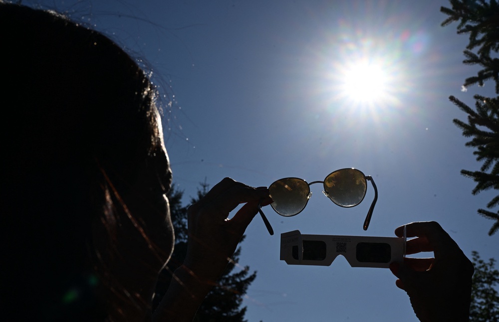 A woman holds a pair of eclipse glasses and sun glasses in front of the sun in Salzburg, Austria on August 12, 2026, ahead of the partial solar eclipse (AFP/Getty)