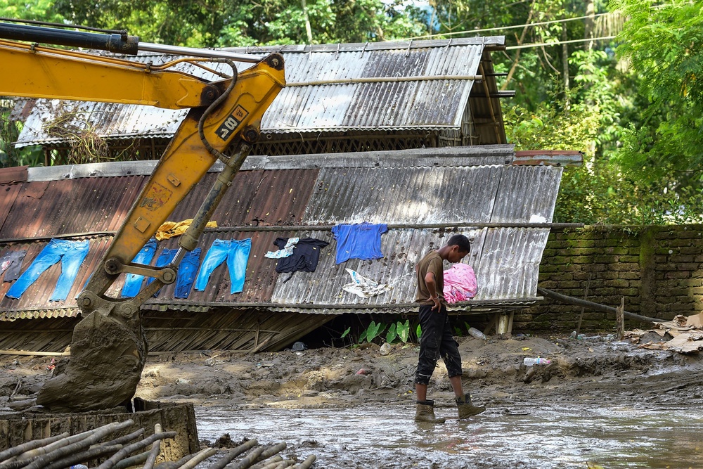 A resident walks past an excavator clearing mud and debris beside a flood damaged house (Getty)