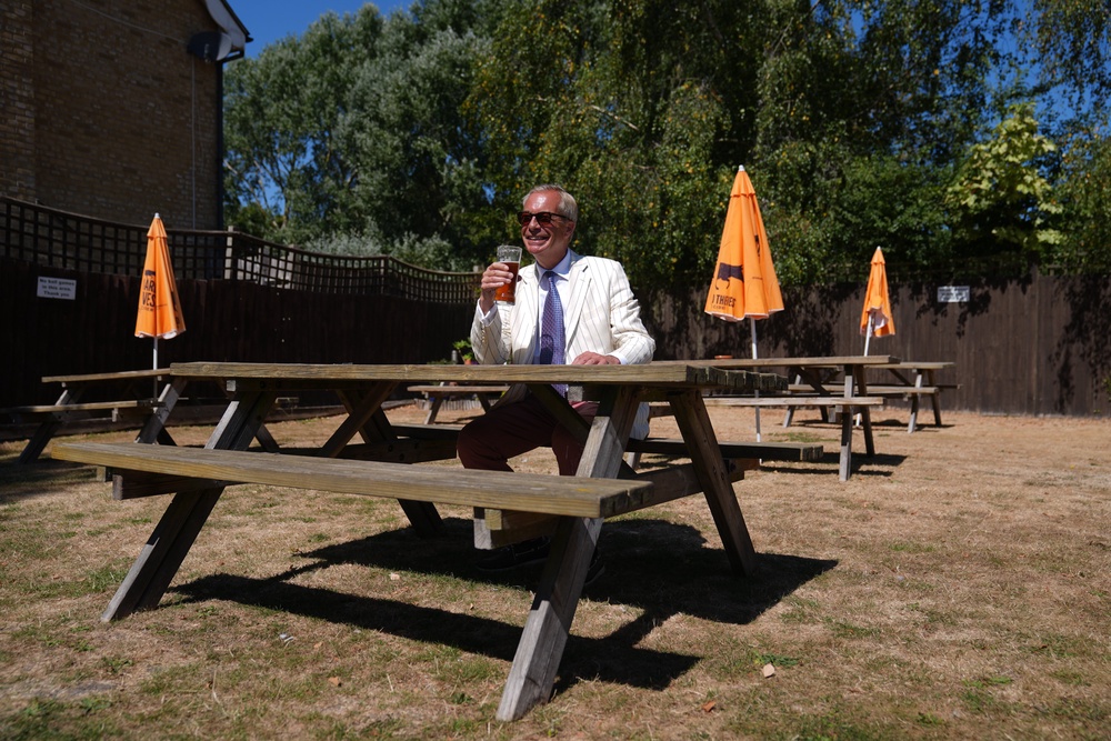 Farage enjoys a pint in the sun on polling day (PA)