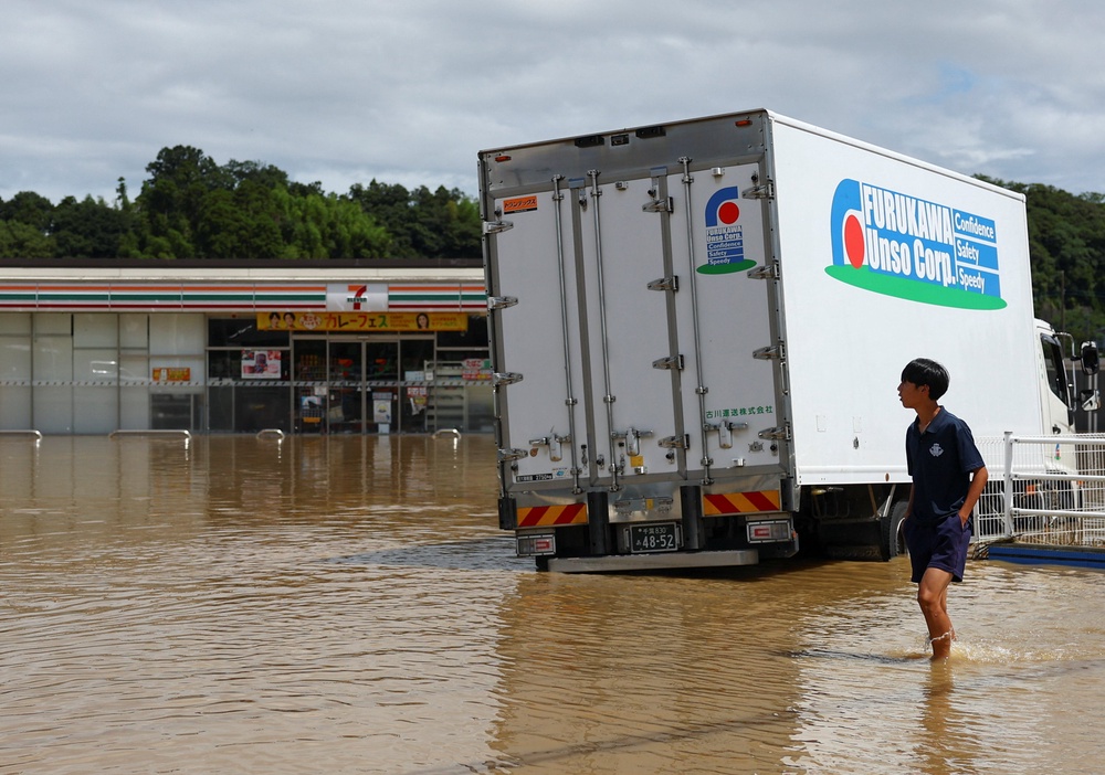 A resident walks near a 7-Eleven store in a flooded area after heavy rain in Oamishirasato, Chiba (Reuters)