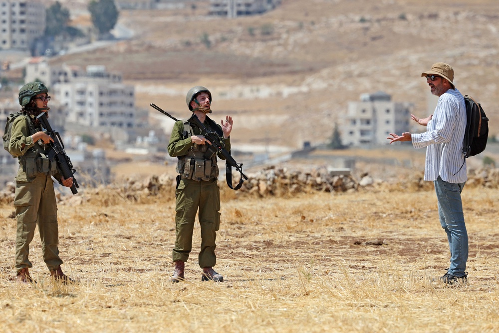 An activist speaks with Israeli soldiers as he accompanies Palestinian landowners to their property, which is at risk of being confiscated by Israeli settlers, in Beit Sahur, south of Bethlehem, in the occupied West Bank on August 14 (AFP/Getty)