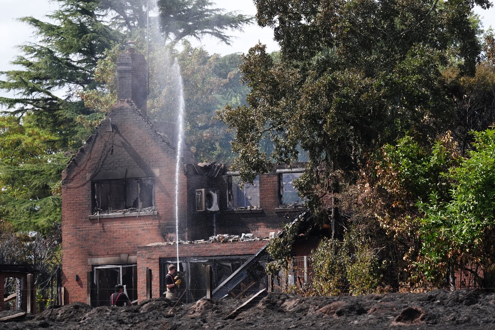 Firefighters spraying water onto the burnt out remains of a house (Jacob King/PA) (PA Wire)
