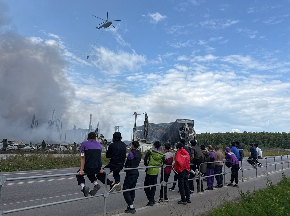 People watch as a water-bombing helicopter flies above the burning Wildberries warehouses following a Ukrainian drone attack, according to the regional governor (Reuters)