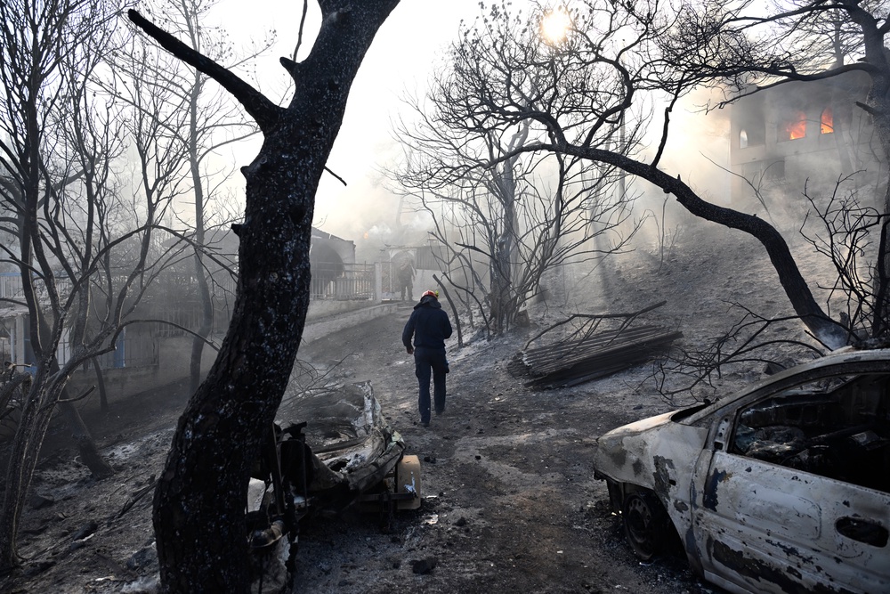 A firefighter walks through a burned area as flames engulf a house during a wildfire on the island of Salamina, west of Athens, Greece (AP)