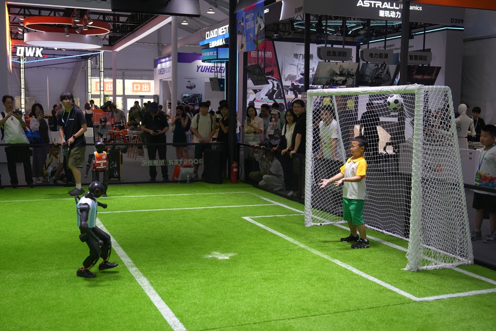 A child reacts on a goal post as he plays soccer with a robot (AP)