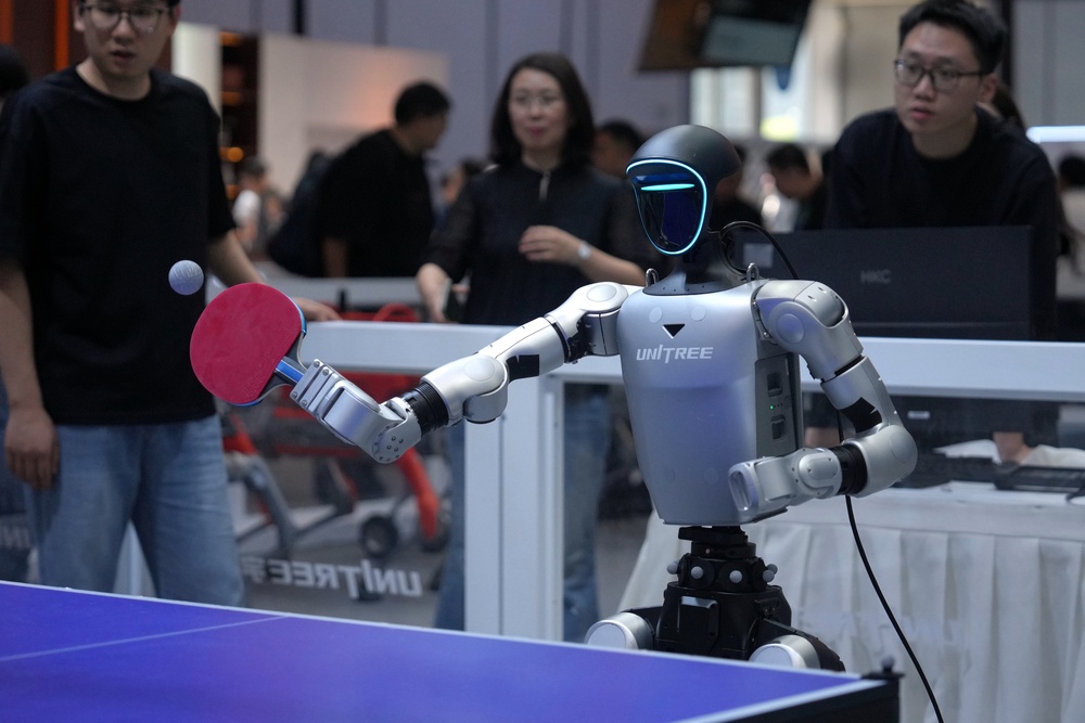 Exhibitors watch a robot play table tennis at a booth of Unitree, one of China's largest humanoid robot makers (AP)