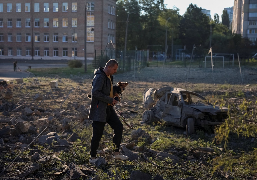 A resident carries a dog as he walks at a site of a Russian missile strike in Kyiv (Reuters)