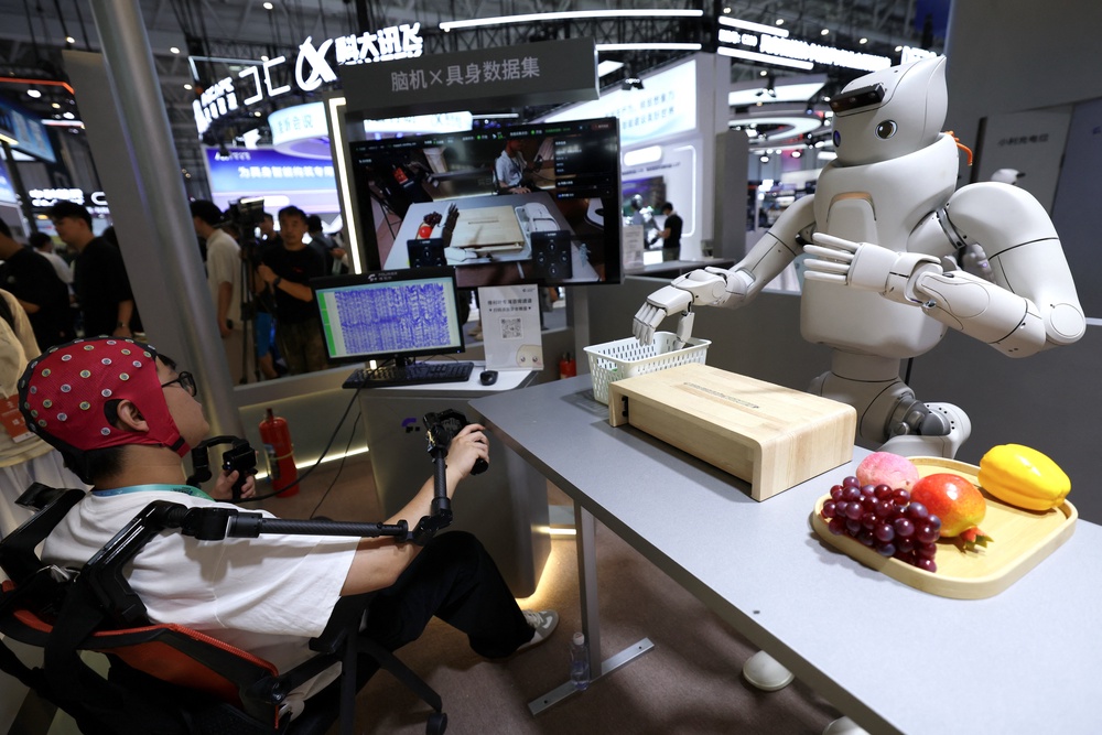 An engineer wears non-invasive brain-computer interface (BCI) head cap to pilot a humanoid robot, at the Fourier Intelligence booth during the 2026 World Robot Conference (Reuters)