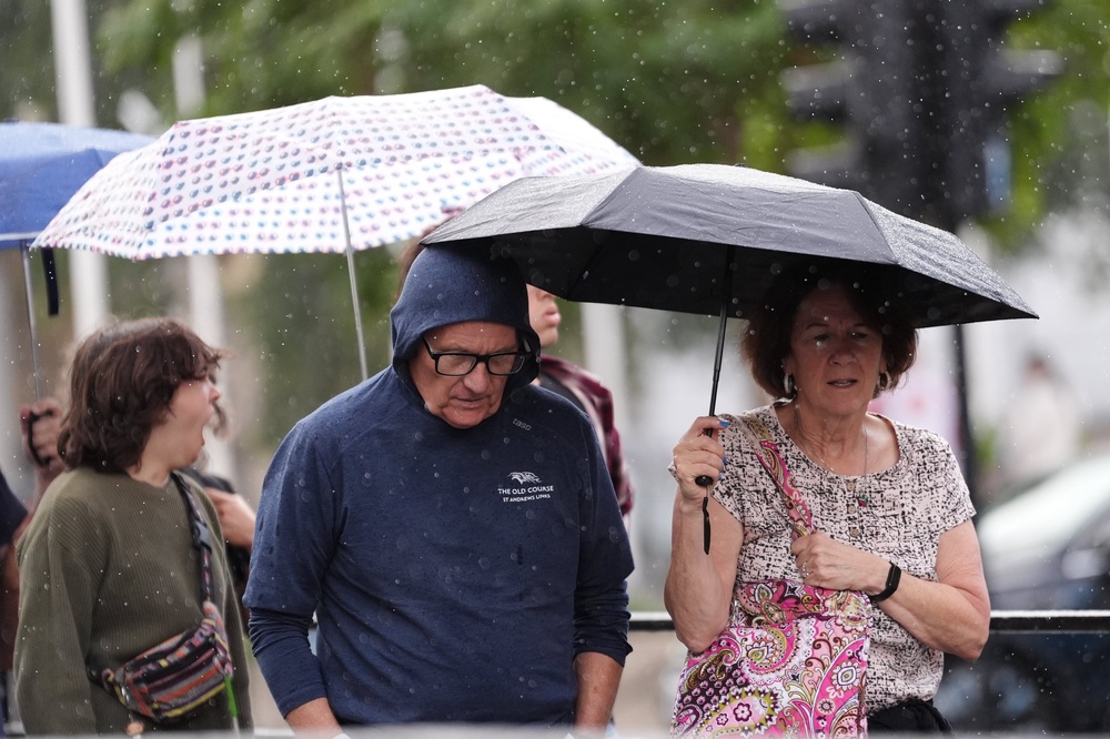 People shelter under umbrellas from the rain in Whitehall, central London (PA)