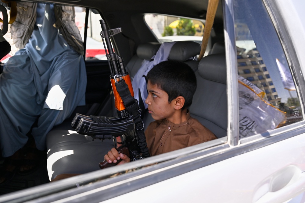A boy holds an AK-style rifle while sitting in a vehicle decorated with Taliban flags during celebrations marking the fifth anniversary of the US withdrawal from Afghanistan and the Taliban’s return to power in Kabul (AP)