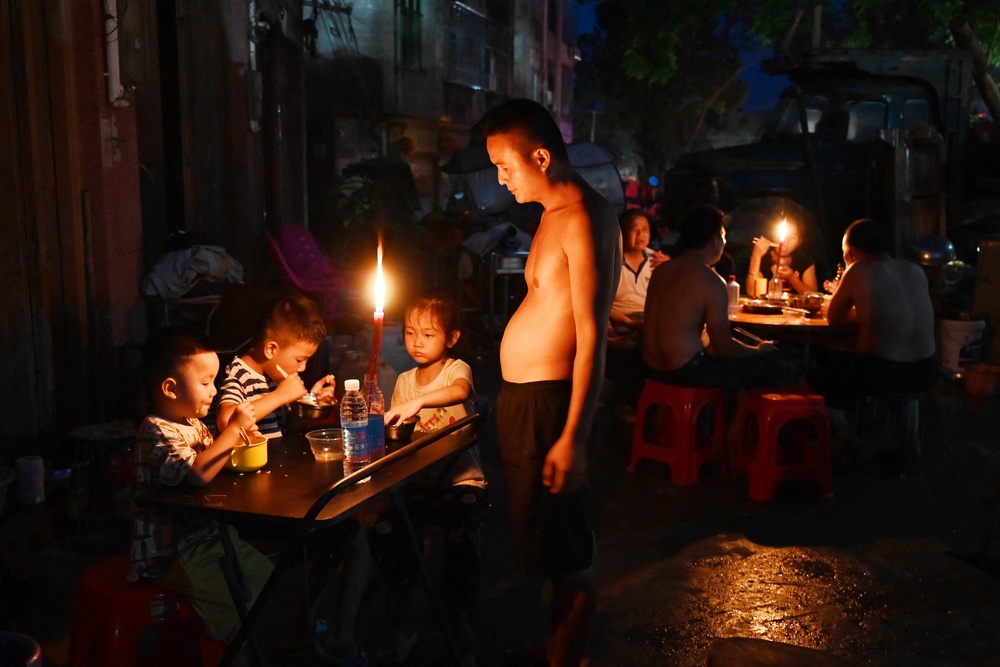 File: A father looks on as children have dinner by candlelight outside a house in Gantang after electricity was knocked out by floodwaters from a collapsed reservoir in China's southwest Guangxi region on 9 July 2026 (AFP/Getty)