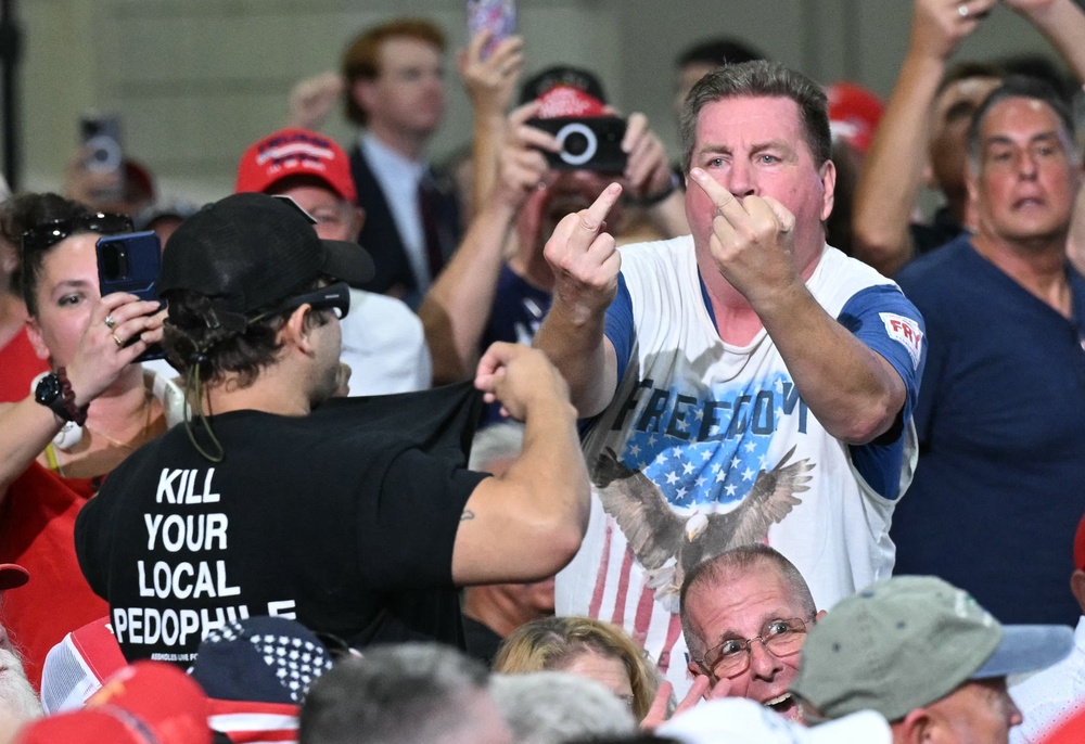 Supporters of US President Donald Trump make rude gestures toward a protester wearing a shirt reading