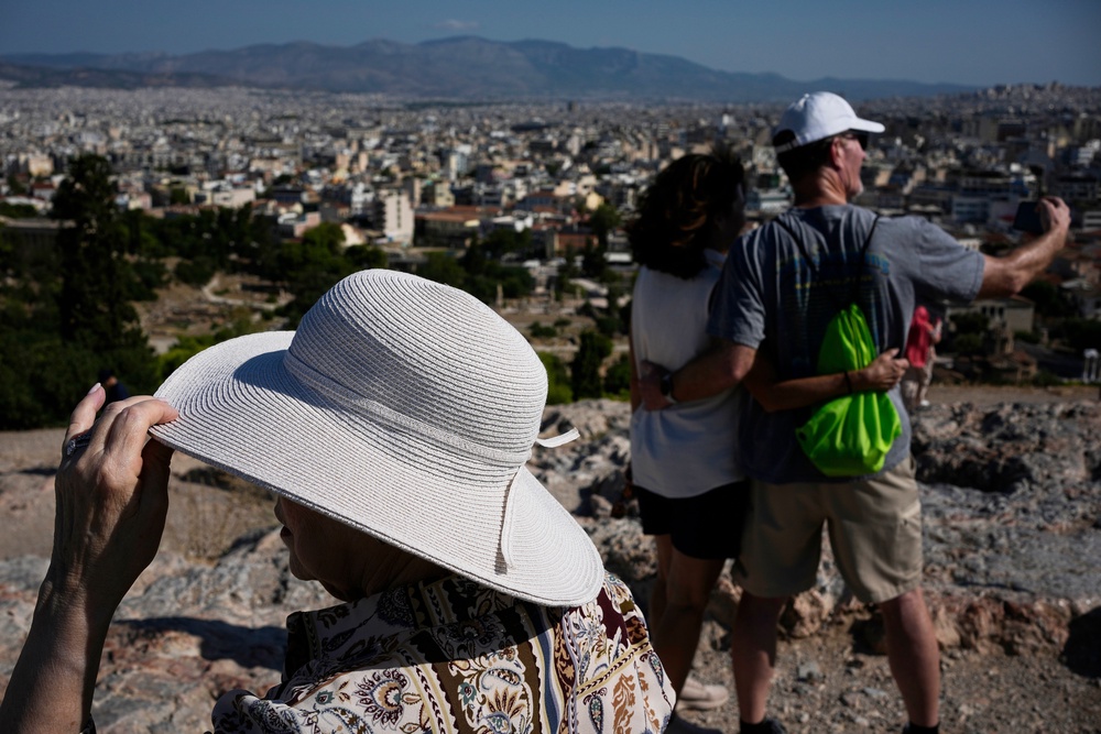 Tourists wearing hats take photographs on the rocky Areios Pagos Hill next to the Acropolis in Athens, Greece, Friday, Aug. 14, 2026. (AP Photo/Thanassis Stavrakis) (Copyright 2026 The Associated Press. All rights reserved)
