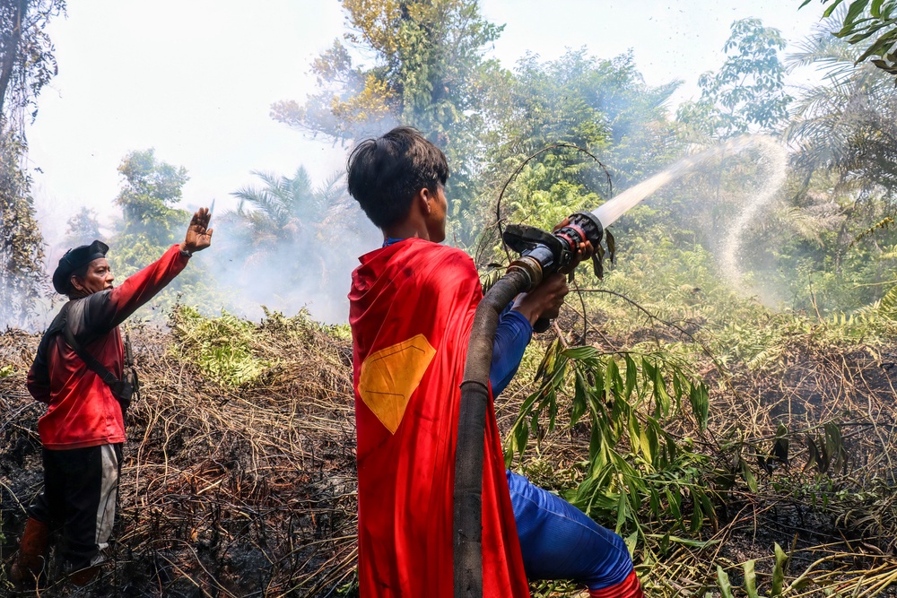 Indonesian student Rudiansyah (R) dressed in a Superman costume helps to extinguish a forest and land fire at Petuk Katimpun in Palangka Raya, Central Kalimantan, on 17 August 2026 (AFP/Getty)