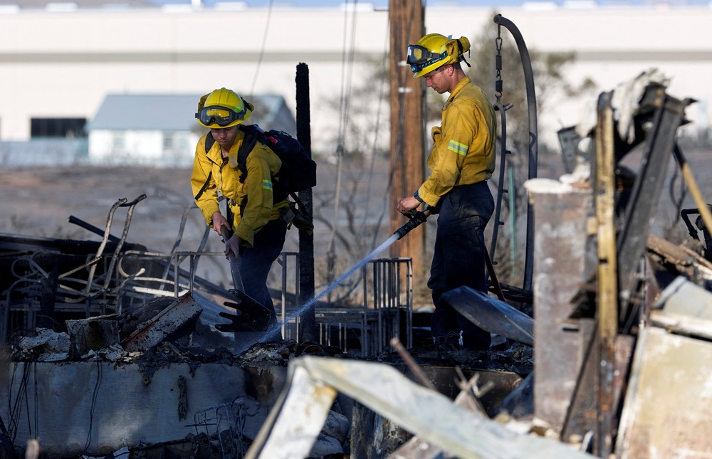 Two firefighters knock down hotspots in the charred remains of a home burned (Reuters)