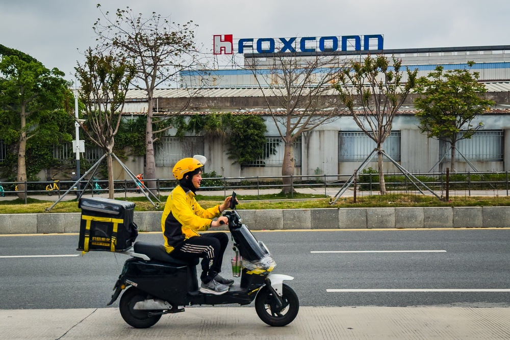 A food delivery rider passes by a Foxconn manufacturing complex in Shenzhen, China (Getty)