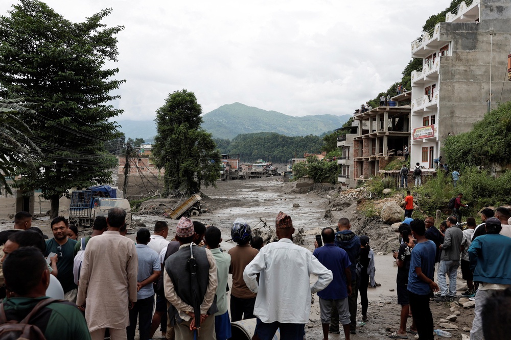 People stand near mud covered houses and a road, following a flash flood at Trishuli (Reuters)