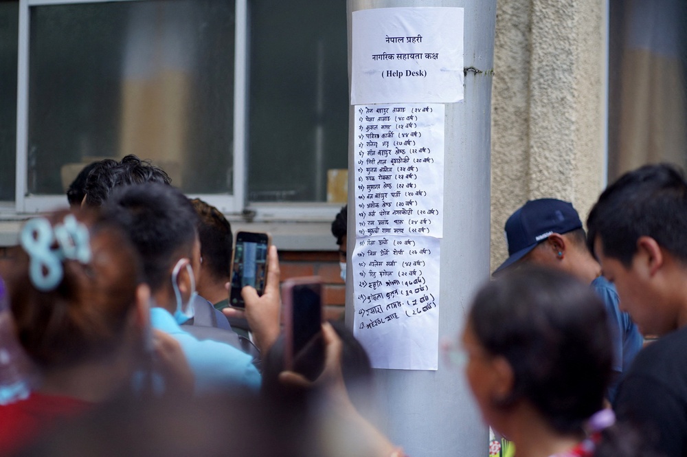 People use their mobile phones to film a list of injured people pasted on a hospital wall following deadly floods in Kathmandu, Nepal, 27 August 2026 (Reuters)