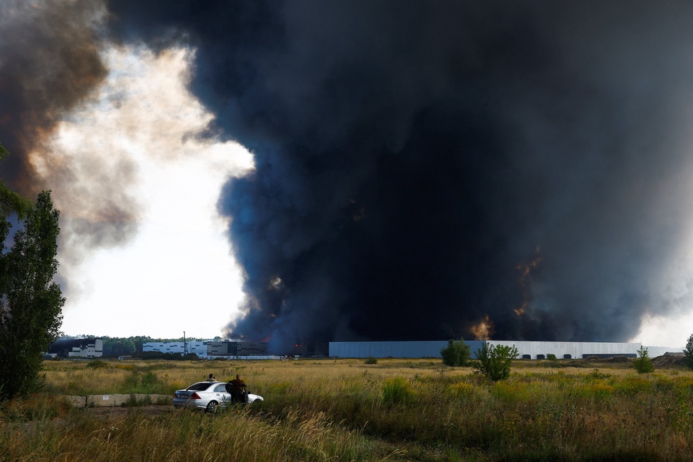 People watch as smoke rises over a warehouse, which was hit by a Russian drone strike, amid Russia's attack on Ukraine, in Kyiv region, Ukraine, August 27, 2026. (Reuters)
