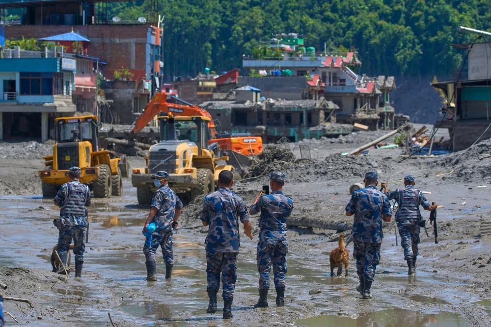 Nepalese policemen watch as earthmovers clear the debris of flash flooding in Nepal’s Nuwakot district (Niranjan Shrestha/AP) (AP)