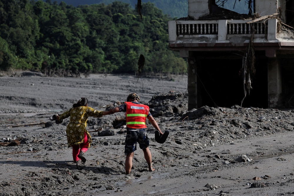 A rescue worker helps a woman move through a muddy road following flash floods and a mudslide in Trishuli, Nepal, on 28 August 2026 (Reuters)