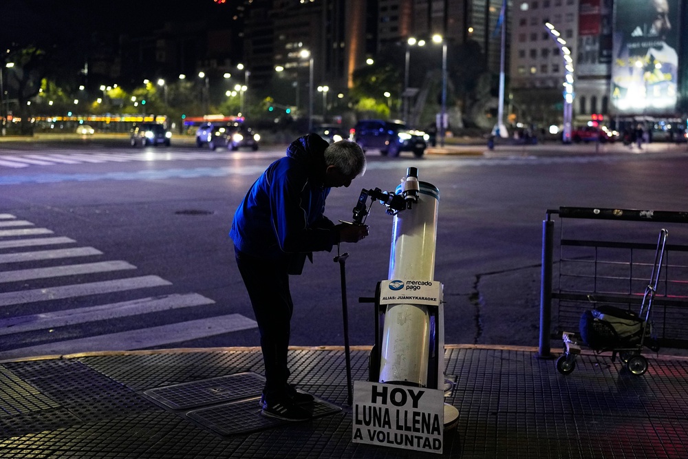 Juan Carlos Sanchez adjusts his telescope as he waits for customers to offer them a chance to view the moon in Buenos Aires, Argentina. (AP)