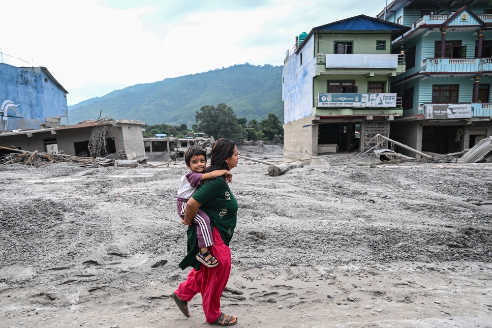 A woman carrying her child walks along a road deluged in sludge after flash floods at Devighat in Nepal's Nuwakot district (AFP/Getty)