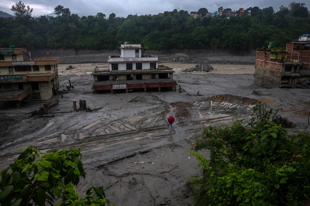A person holds an umbrella as he stands in front of damaged buildings after flash floods and a mudslide, in Trishuli, Nuwakot district, Nepal (Reuters)