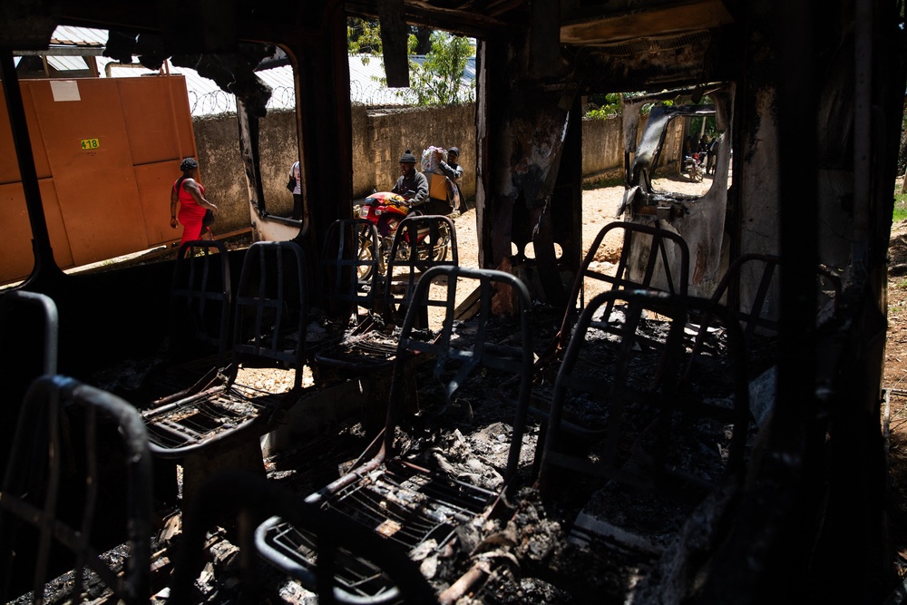 Pictured: People walk past the remains of a charred vehicle following overnight violence in Kenscoff, a neighborhood near Port-au-Prince, Haiti, on August 24 (AFP via Getty Images)