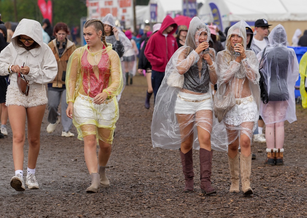 Festivalgoers shelter from the rain in plastic ponchos as they walk through the muddy site at the Reading Festival (Jeff Moore/PA) (PA Wire)
