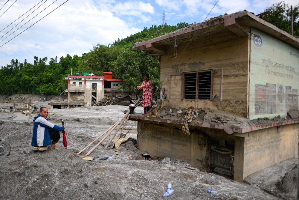A woman (R) stands atop her house covered in mud in the aftermath of flash floods at Baireni in Nepal's Dhading district on 30 August 2026 (AFP/Getty)